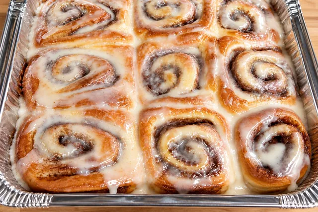 A pan of nine Rodeo Bites cinnamon rolls under icing, on a butcher block